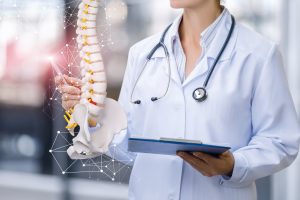 A,Medical,Worker,Shows,The,Spine,On,Blurred,Background.
